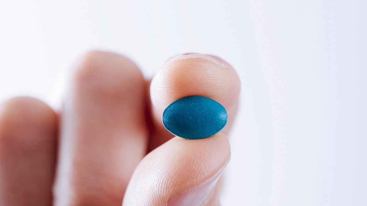 A hand holding the little blue pill of viagra