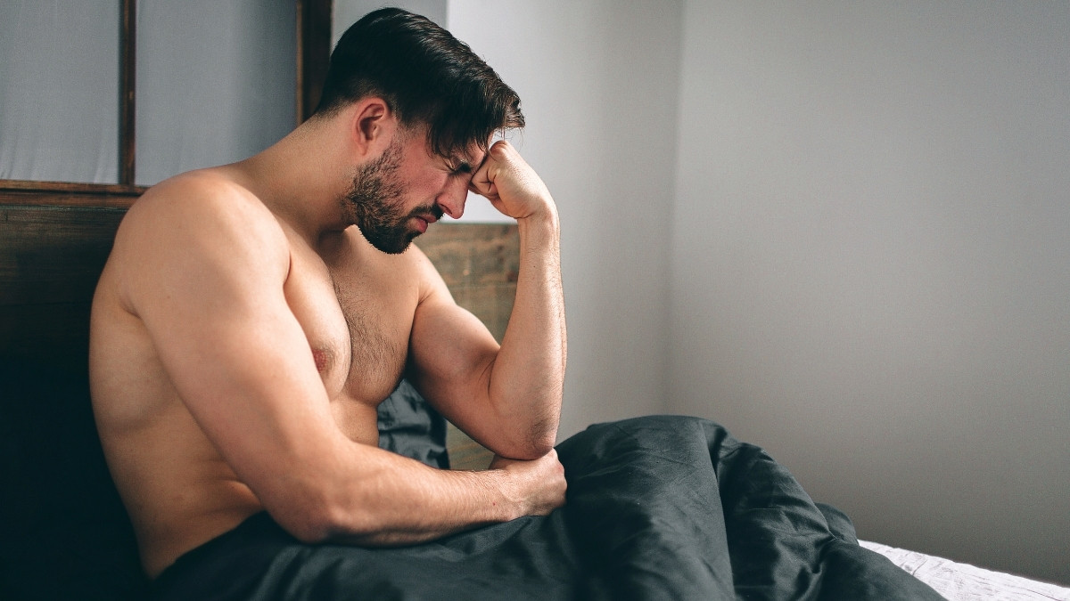 Sad man sitting on bed suffering from erectile dsyfunction